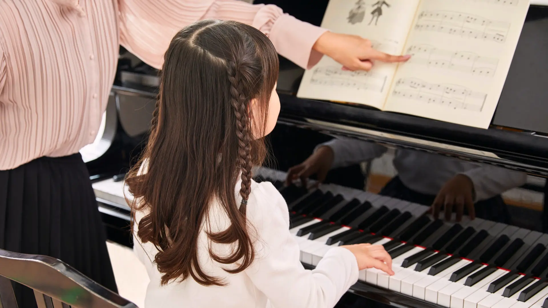 A young student learning piano with her teacher